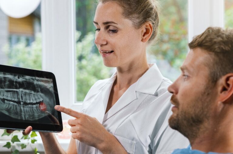 Zahnarzt, der seinem Patienten eine Röntgenaufnahme mit einem impaktierten Weisheitszahn zeigt und erklärt