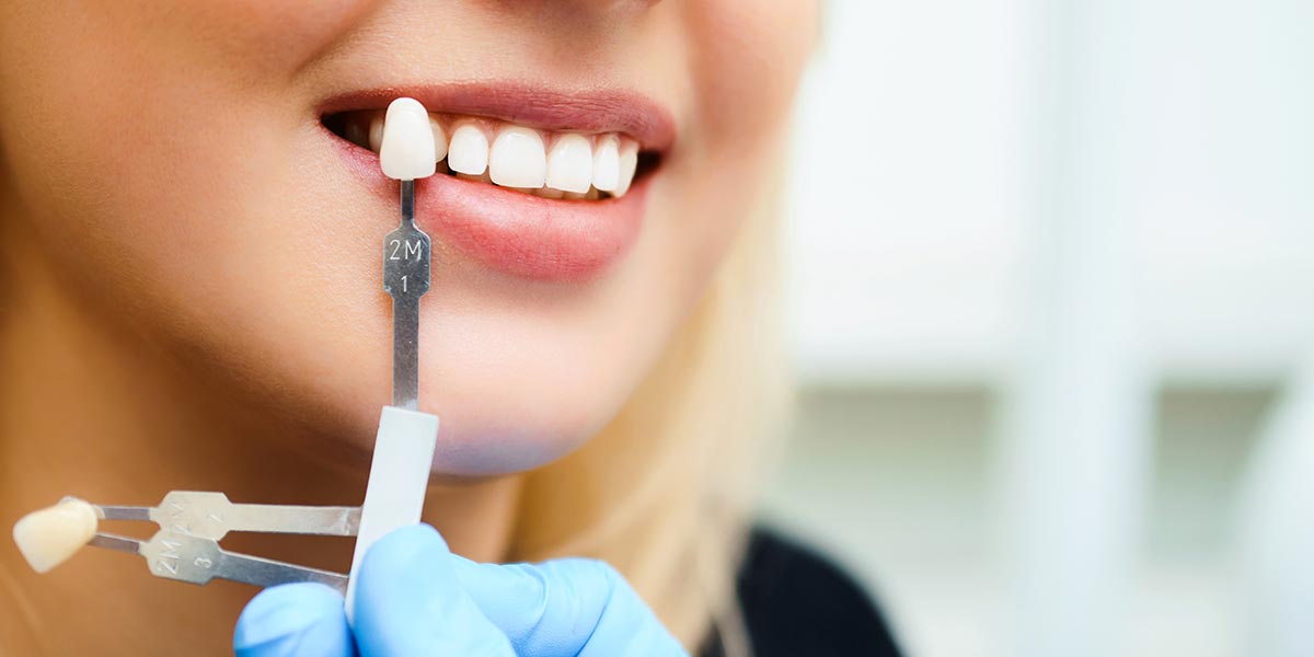 Frau hält sich Zahnprothese vor lächelnden Mund